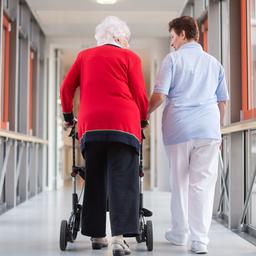 Eine Pflegerin geht mit einer Bewohnerin des Pflegeheims und einem Rollator über den Flur.