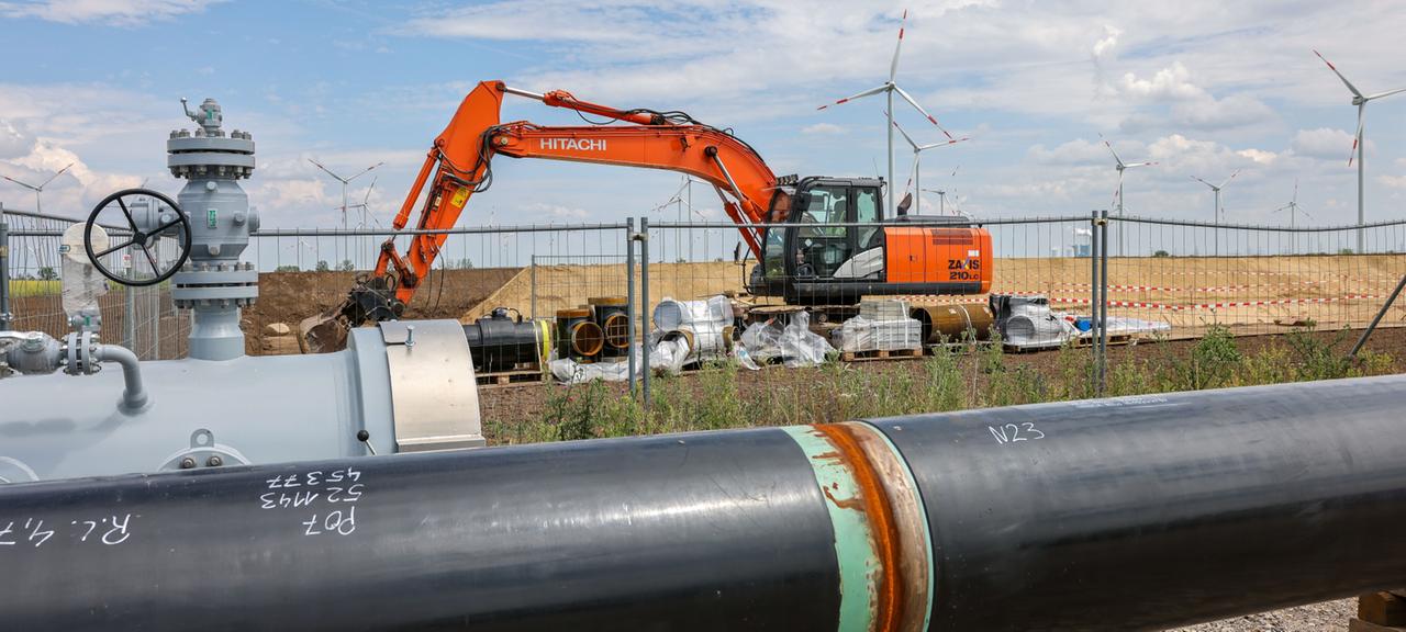 Die Rohre einer künftigen Wasserstoffleitung liegen vor der Kulisse eines Windparks. 