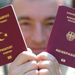Ein türkischer und eine deutscher Reisepass werden von einem Mann in die Kamera gehalten.