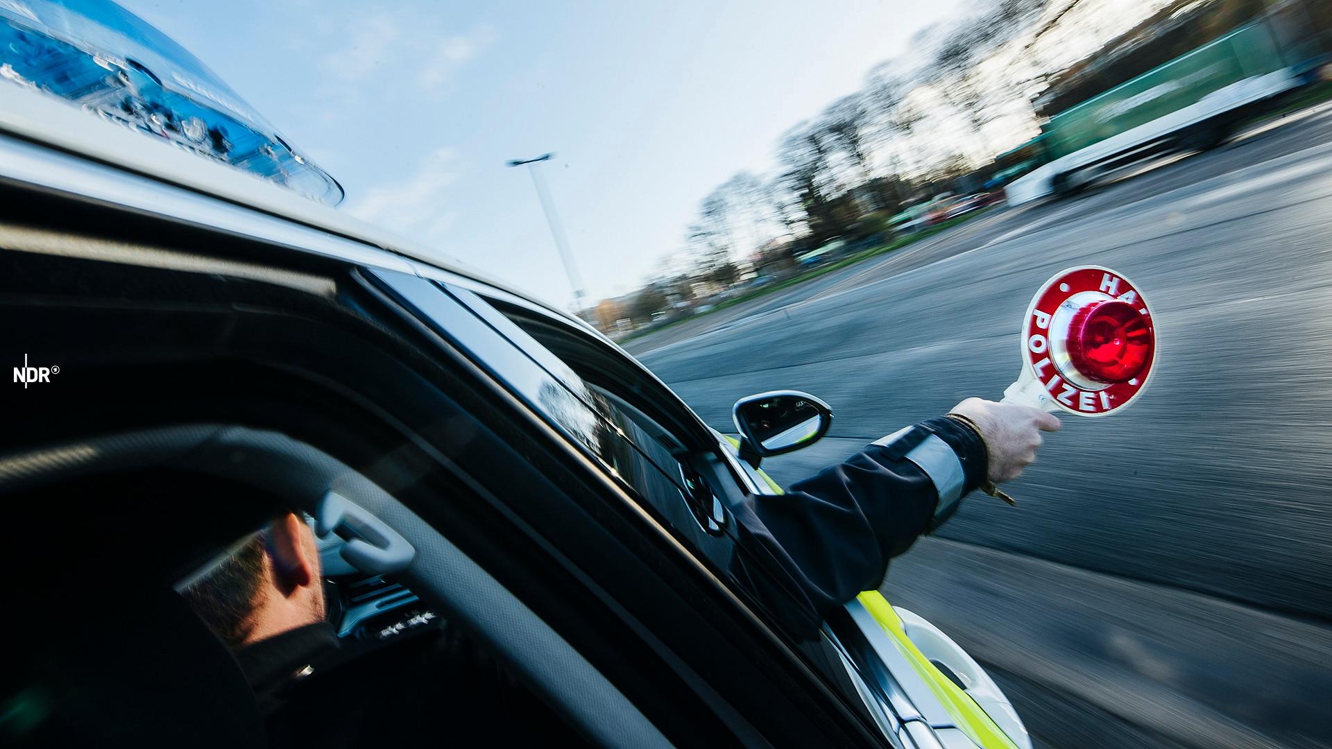 Ein Polizist hält eine rote Polizeikelle aus dem Beifahrerfenster eines Streifenwagens heraus. 