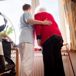 Eine Seniorin und eine Pflegerin schauen zusammen aus einem Fenster im Wohnbereich eines Pflegeheims.