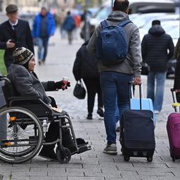 Eine Frau in einem Rollstuhl hält eine Becher für Almosen in der Hand. 