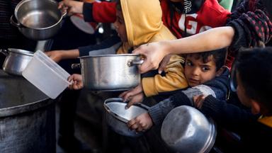 Kinder warten in Rafah im Gazastreifen inmitten einer Menschenmenge mit leeren Töpfen in der Hand an einer Essensausgabe.