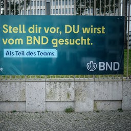 Ein Arbeiter säubert ein Plakat der neuen Imagekampagne des Bundesnachrichtendienstes (BND) mit der Aufschrift "Stell dir vor, du wirst vom BND gesucht" am Zaun der Zentrale des Dienstes.