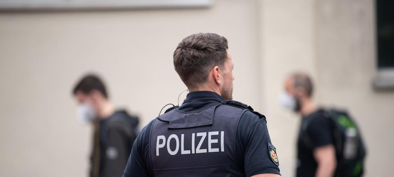 Auf dem Rücken eines Mannes steht "Polizei", der Polizist schaut zur Seite. Im Hintergrund gehen Menschen vorbei.