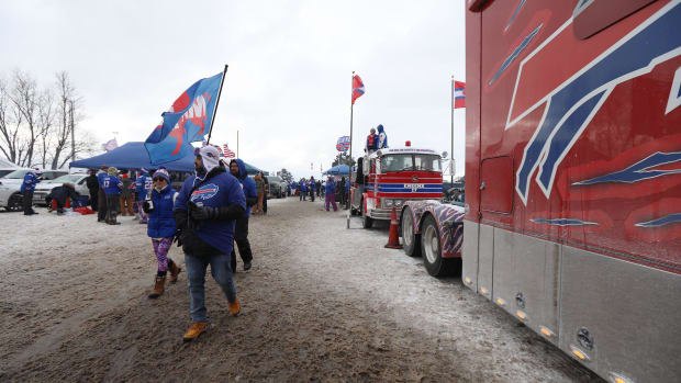 A Bills fan carrying a Bills Mafia flag leaves a parking lot full of tailgaters and heads to the stadium.