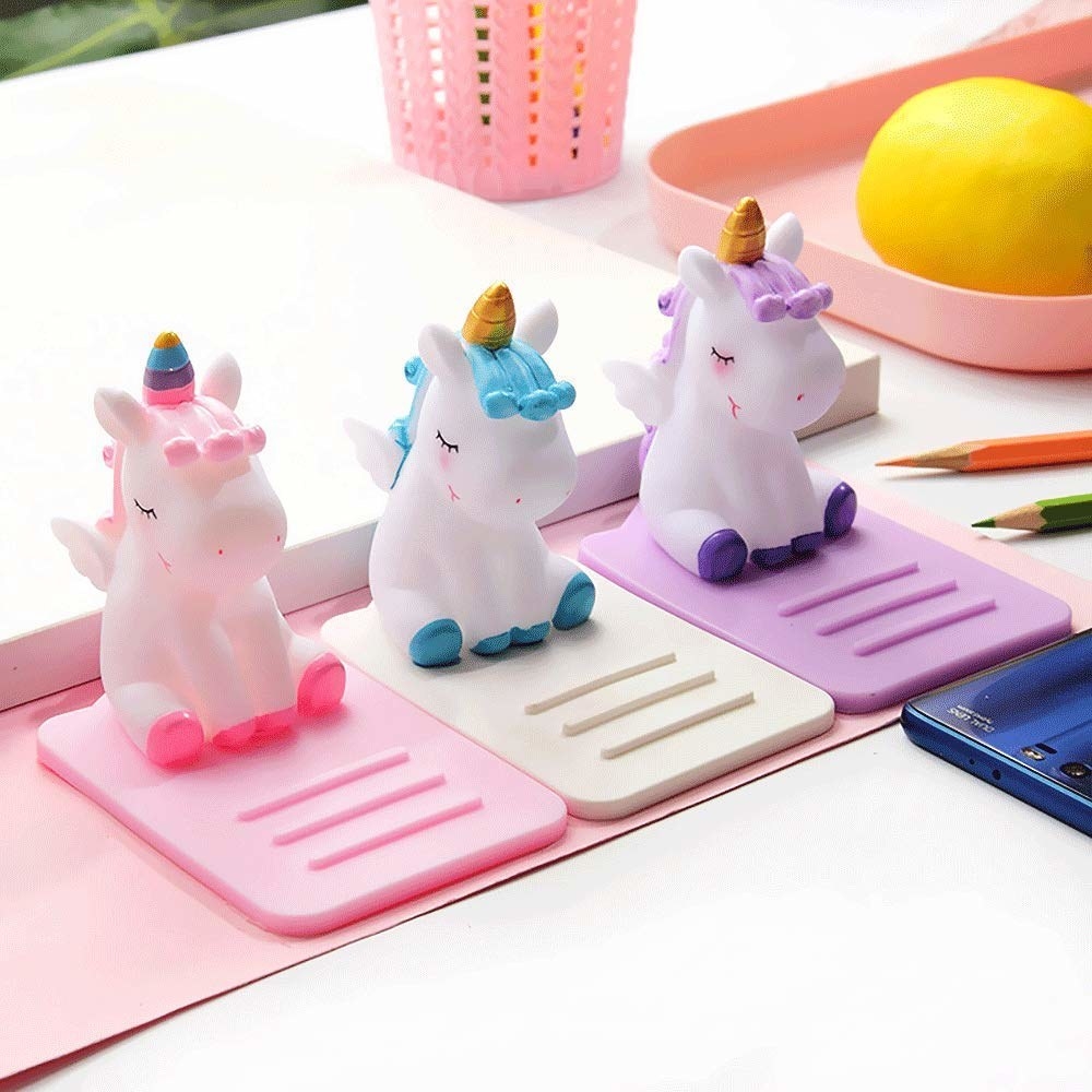 A set of three matching phone holders with ridges that let you lean your phone on little chubby cartoon-y unicorns on the edge of them 