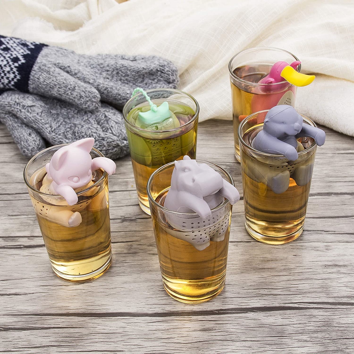Five infusers shaped like a cat, a hippo, a sloth, an owl, and a platypus in clear tea glasses. 