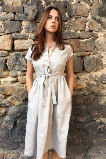 a model wearing a gray linen dress with their hands in the side pockets and a sash-tie belt 