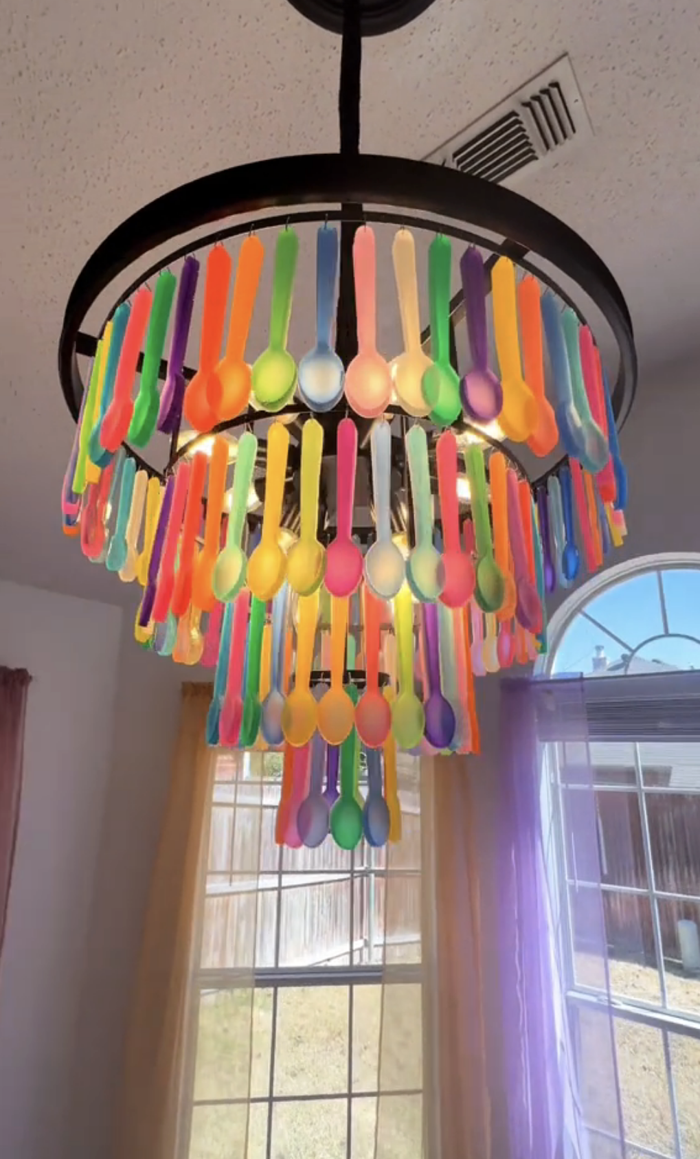 A closer shot of the chandelier made of colorful spoons hanging indoors, creating a unique decoration