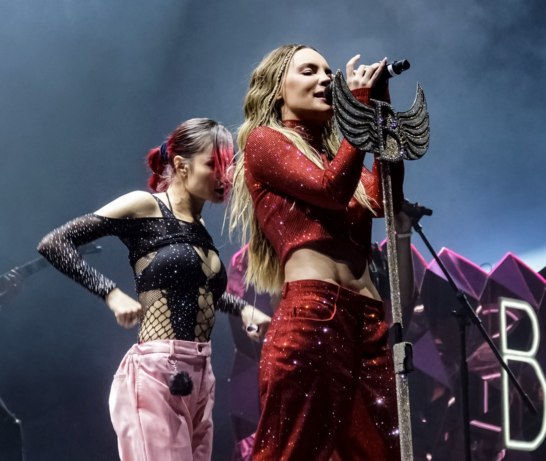 Cantante con atuendo rojo de lentejuelas actuando en un concierto con otra persona bailando a su lado