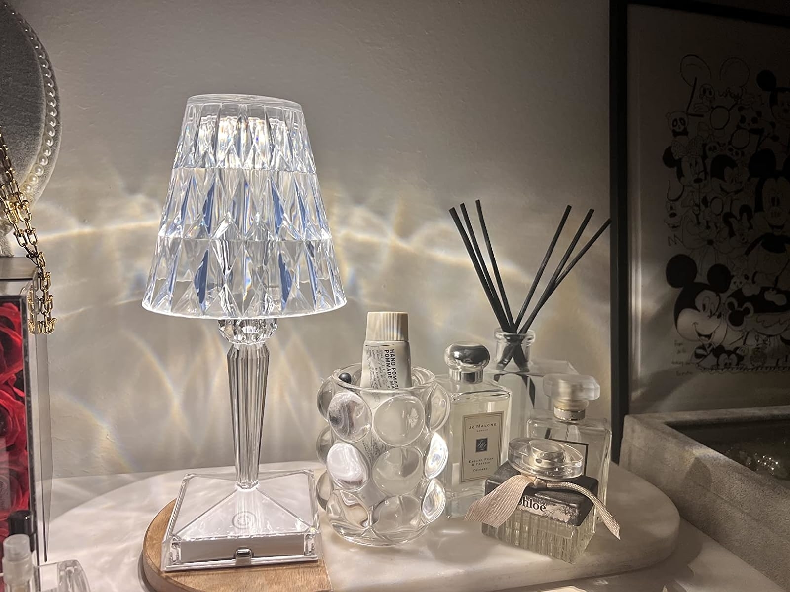 Crystal lamp beside beauty products including Jo Malone and Dior on a vanity shelf with a Mickey Mouse art piece in the background