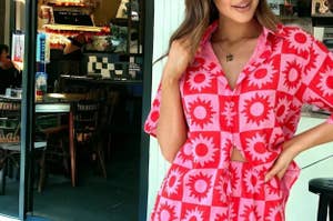 Woman in vibrant tropical print outfit with shorts and sunglasses, standing by a coastal backdrop for a style feature