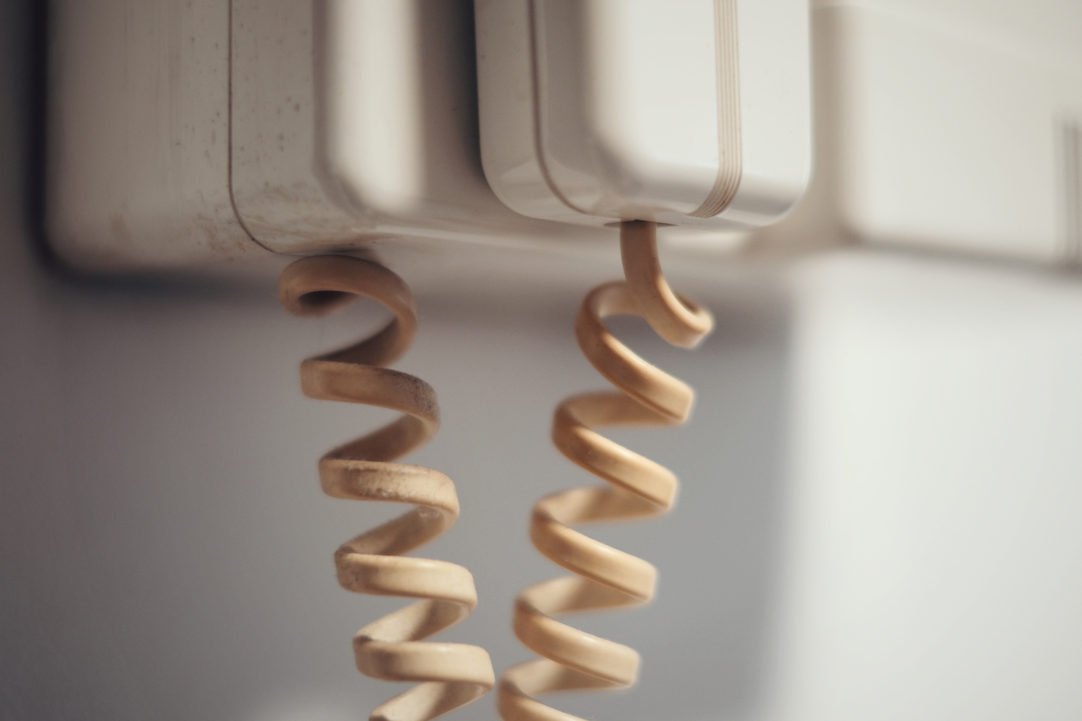 Retro telephone receiver with curled cord hanging on a wall-mounted base. There are no people in the image. Category: Internet Finds