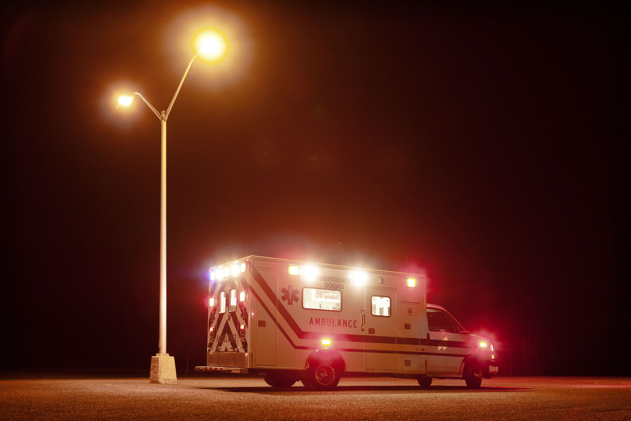 Ambulance parked under a streetlight at night with its lights on