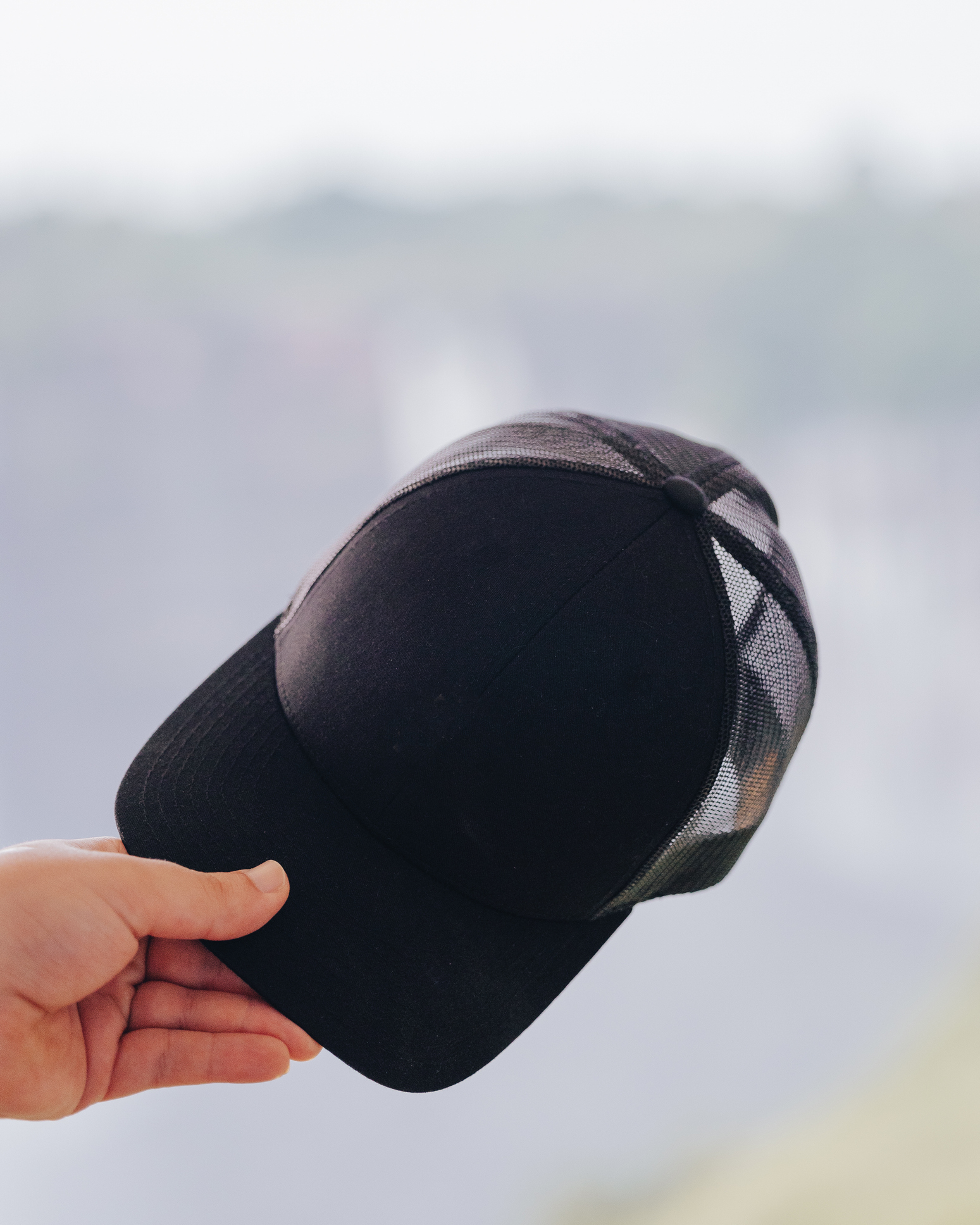 A hand holding a black baseball cap with a mesh back