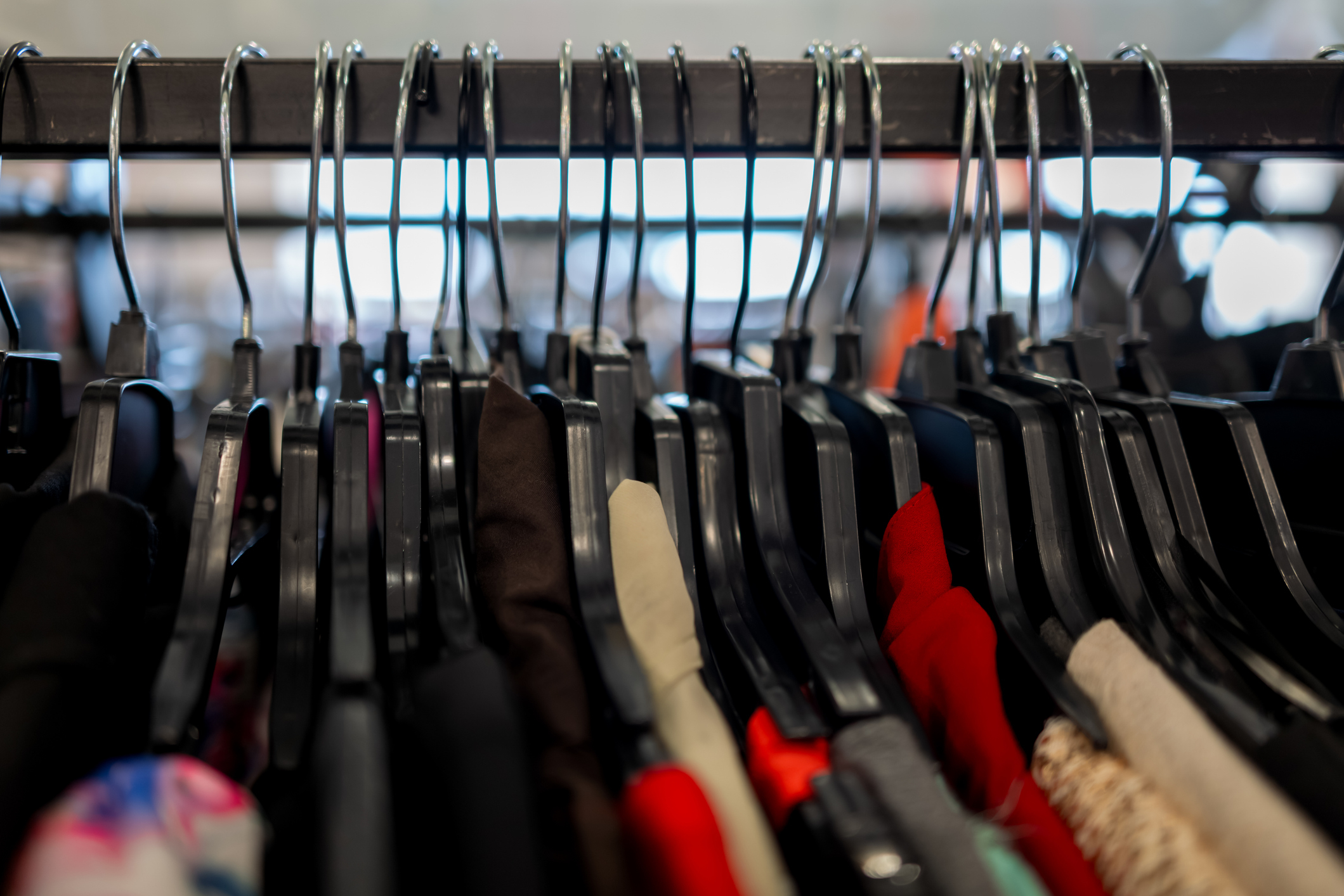 Clothes on hangers arranged closely together on a rack. The image features various fabrics and styles, symbolizing a collection of garments in a store or closet