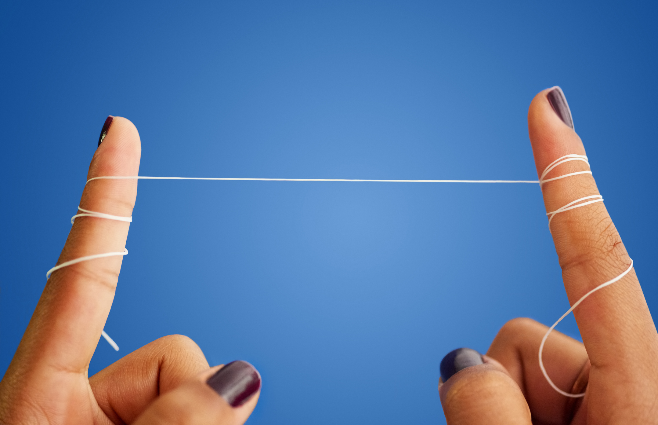 Close-up of two hands with fingers wrapped in floss, pulling it tightly between them