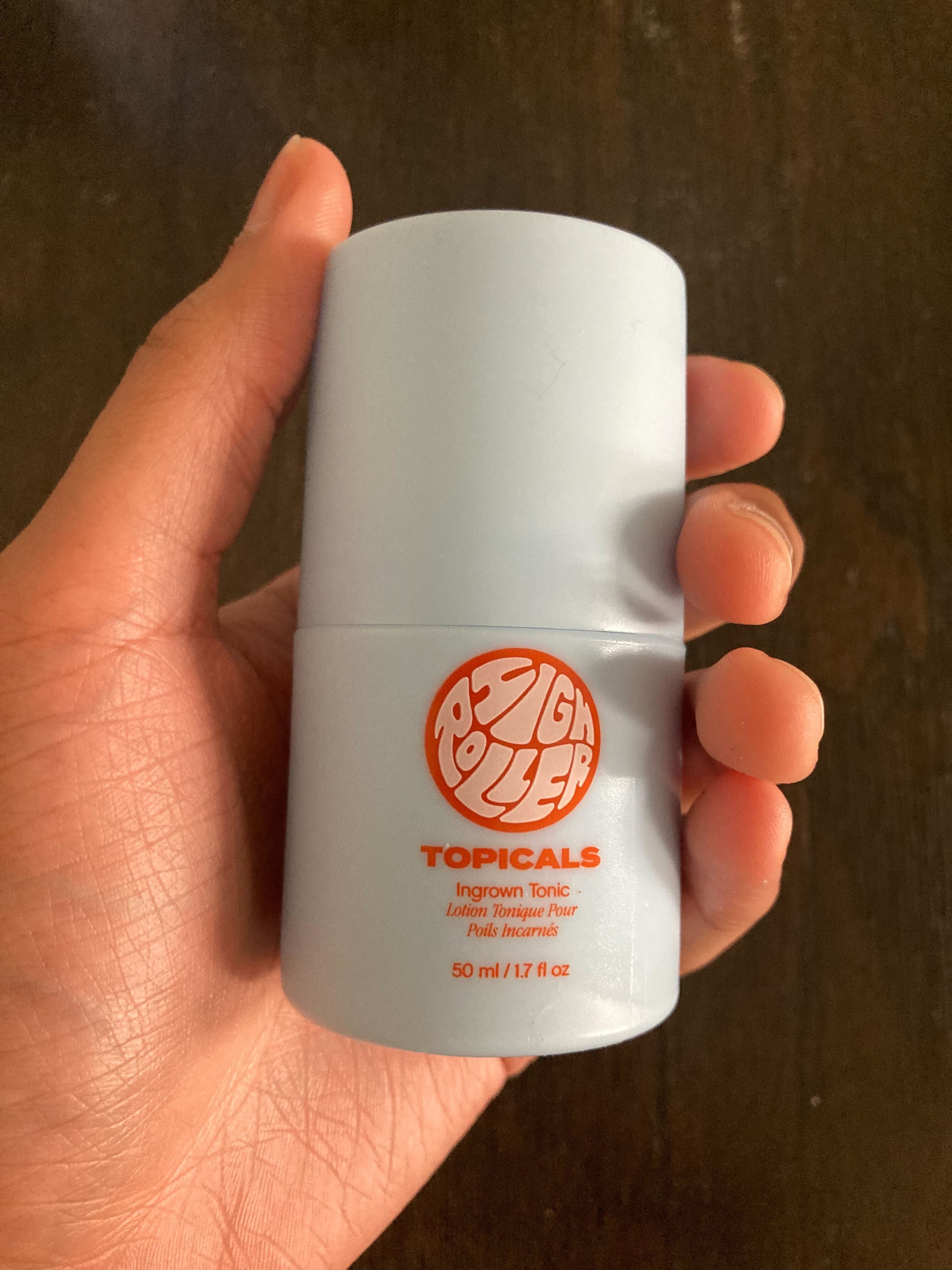 Hand holding a container of &quot;Zit Roller&quot;, an ingrown tonic by Topicals. The label mentions it targets ingrown hairs and lists the volume as 50 ml (1.7 fl oz)