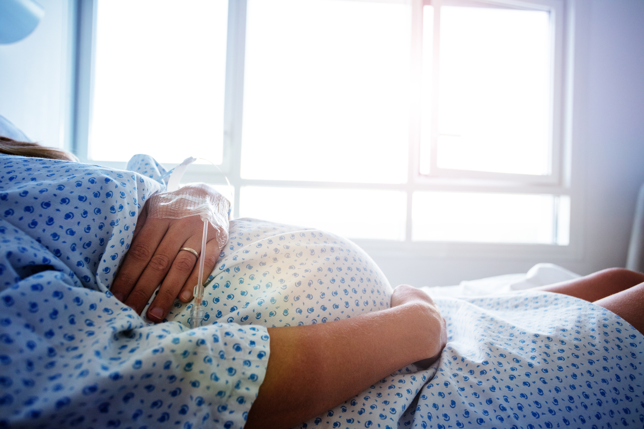 A pregnant woman lying in a hospital bed, wearing a gown, with hands resting on her belly