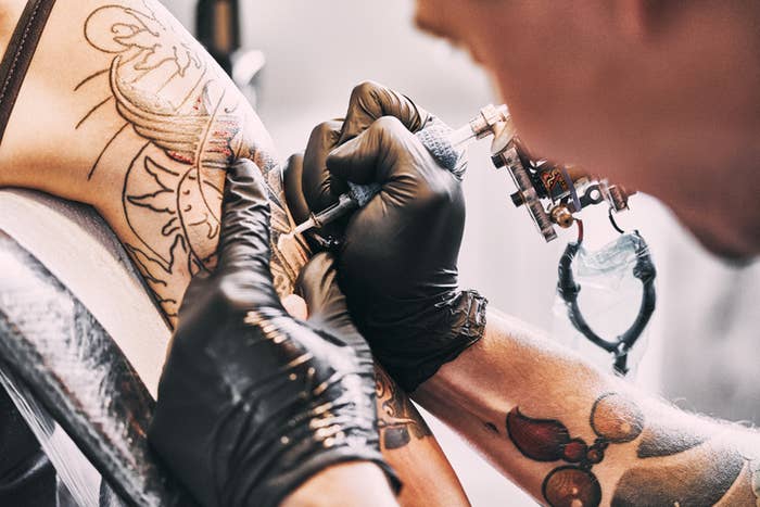 Close-up of a tattoo artist&#x27;s gloved hands inking a sun and moon design on a person&#x27;s upper arm