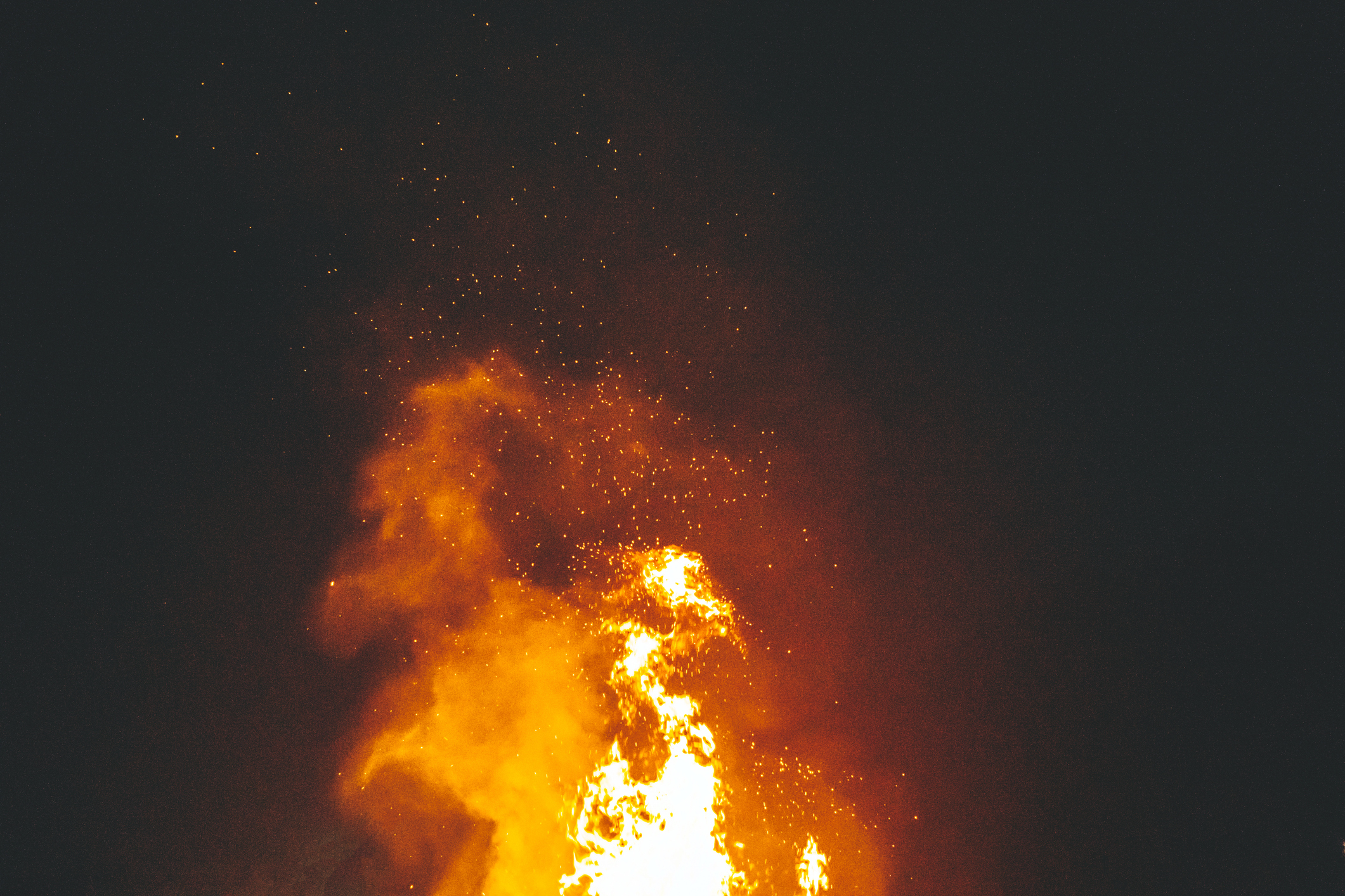 A large bonfire burns intensely against the night sky with sparks flying upwards