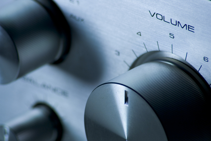 Close-up of a stereo system&#x27;s volume control knob, set to a medium level, reading &quot;Volume.&quot; Other control knobs are partially visible