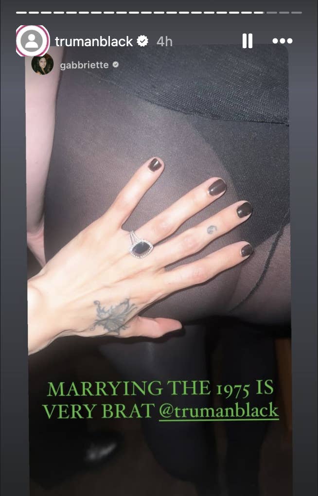 Gabriette&#x27;s hand with tattoo and ring resting on a person&#x27;s leg. Text reads: &quot;MARRYING THE 1975 IS VERY BRAT @trumanblack&quot;