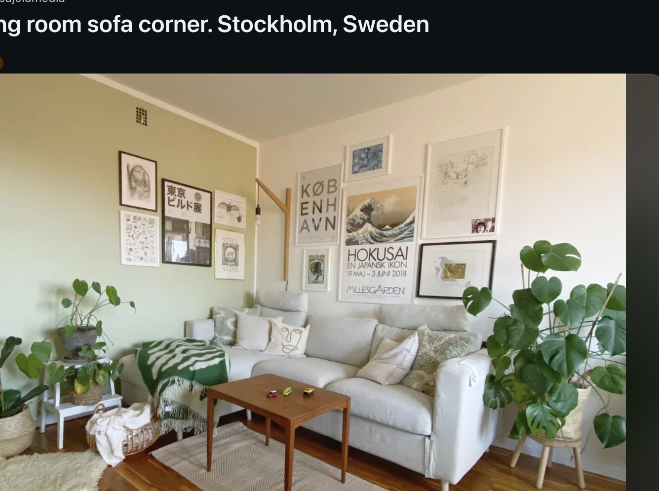 A cozy living room corner in Stockholm, Sweden, featuring a beige sofa adorned with cushions, a small wooden table, and green plants. Wall art is displayed above the sofa