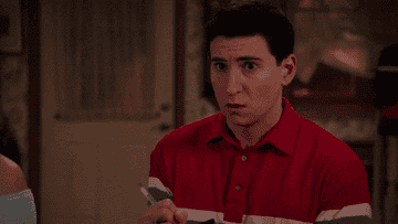 A man in a red and white striped polo shirt holds a pen, appearing surprised, within a domestic interior setting