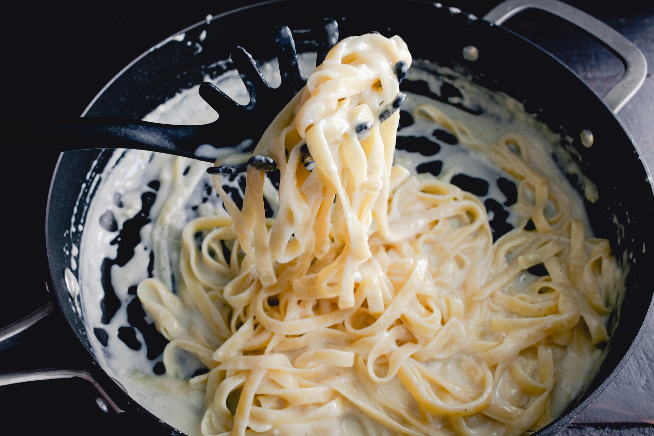 A close-up of creamy fettuccine alfredo being lifted from a pan with a pasta server