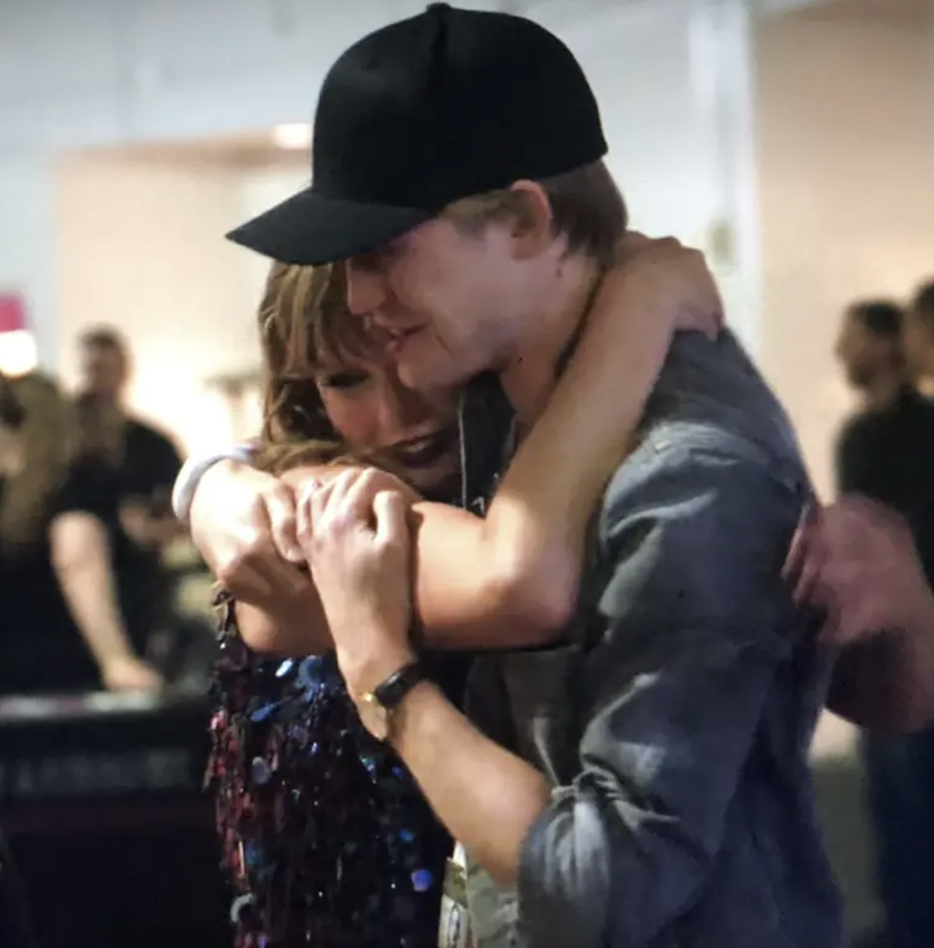 Taylor Swift and Joe Alwyn, embracing each other. Taylor is wearing a sparkly outfit, while Joe is in a casual shirt and cap