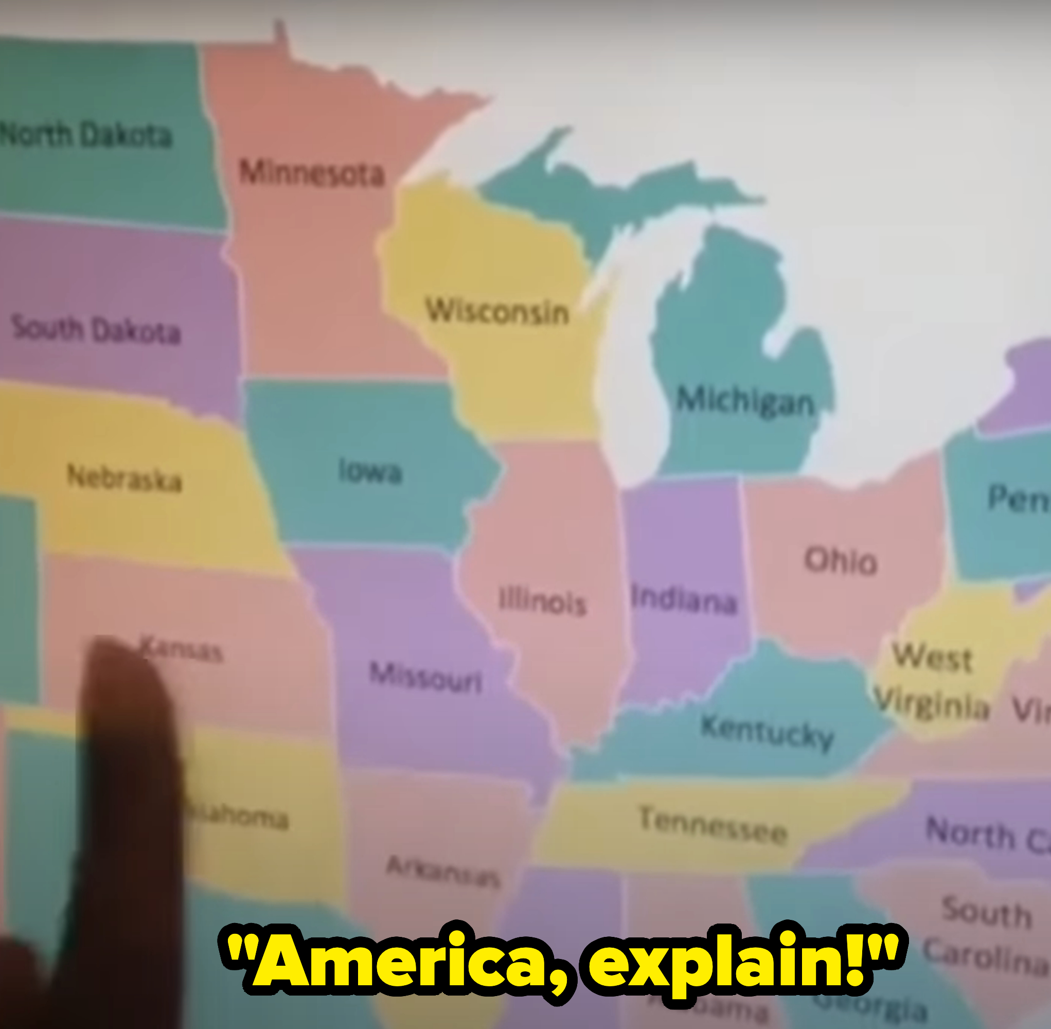 A hand points to a map of the United States, with caption, &quot;America, explain!&quot;