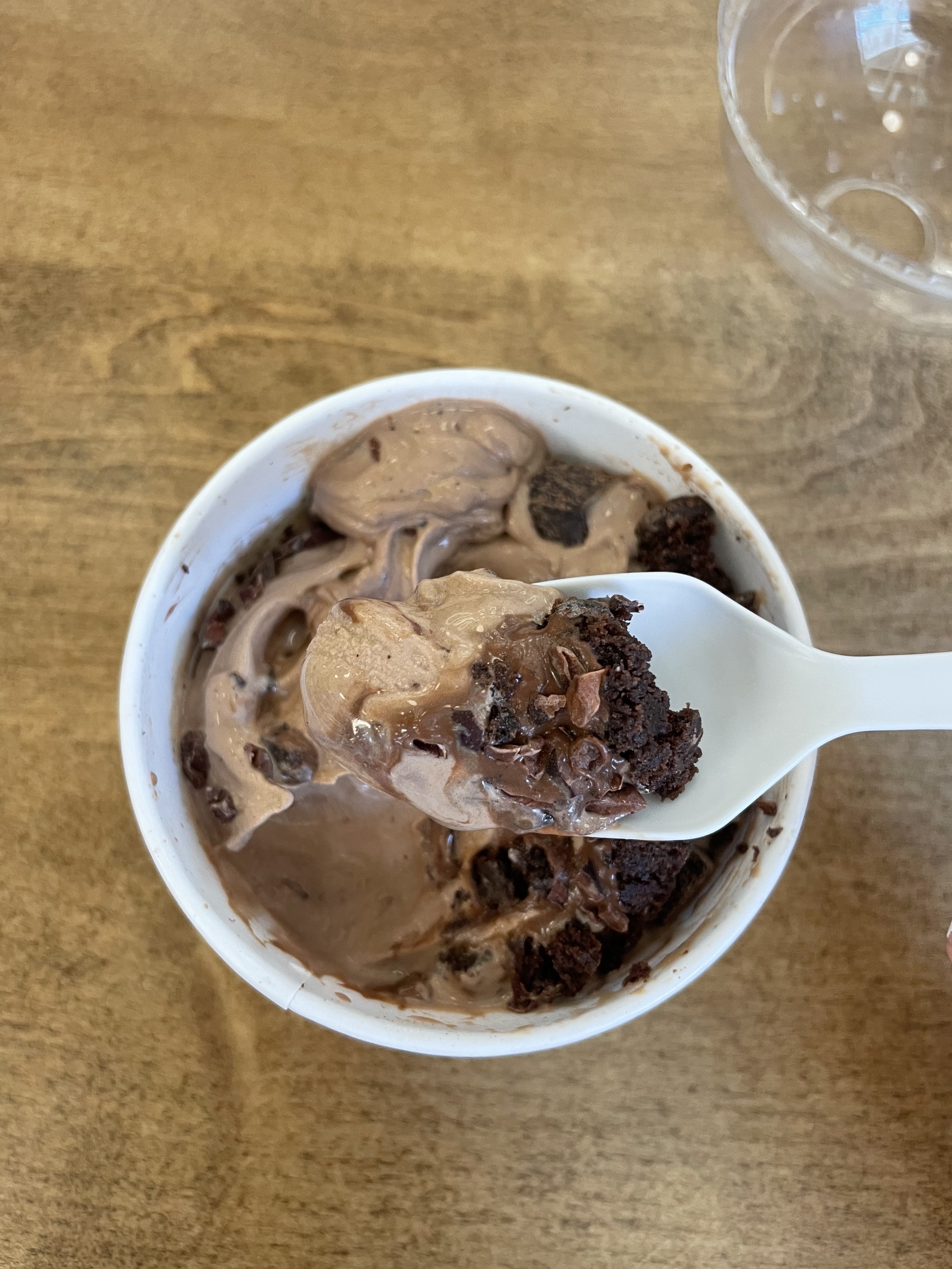 A spoonful of chocolate ice cream with brownie chunks is lifted from a white cup