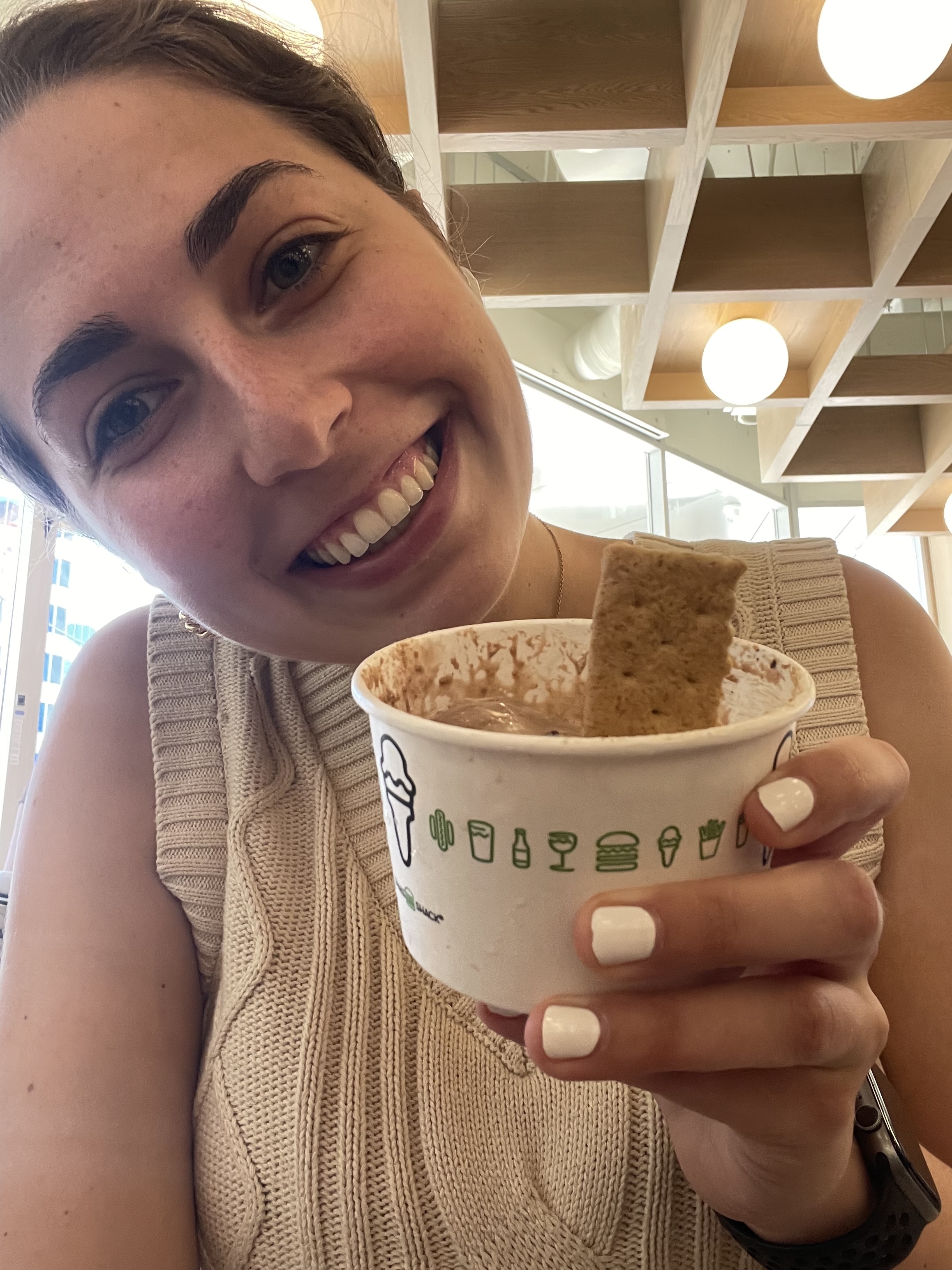 A woman with a smile holds a cup of Shake Shack ice cream with a cookie