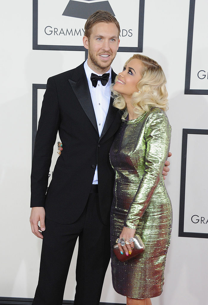 Calvin Harris in a tuxedo and Rita Ora in a shiny dress pose together on the Grammy Awards red carpet