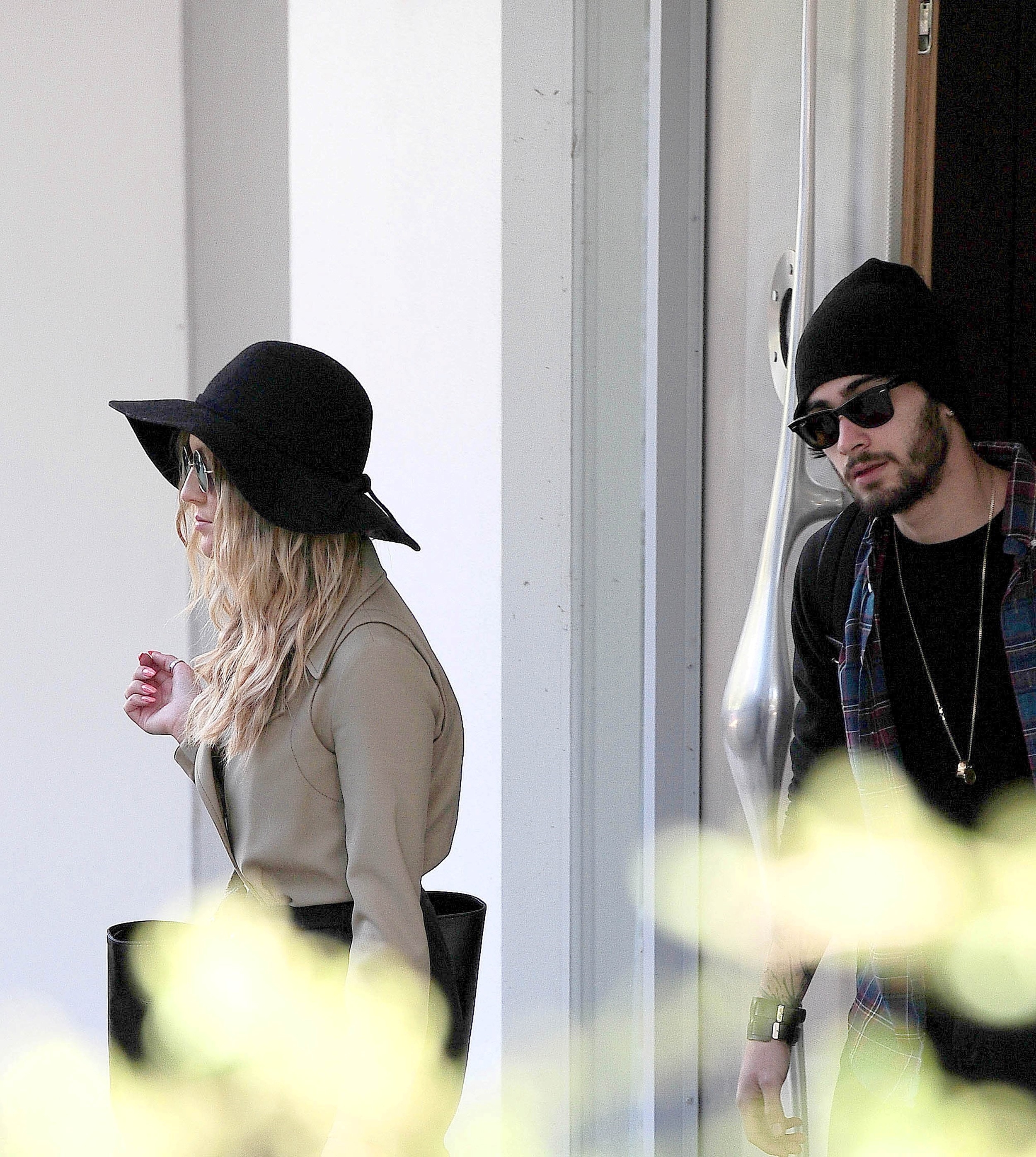 Zayn Malik and Perrie Edwards are pictured together; Perrie wears a wide-brimmed hat and sunglasses, while Zayn wears a beanie and dark sunglasses