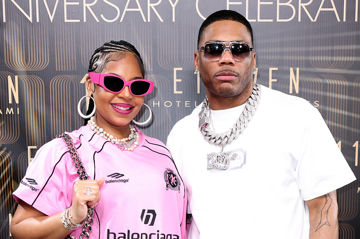 Ashanti in a pink Balenciaga dress and sunglasses, and Nelly in a white t-shirt and blue pants, posing together at a celebration event