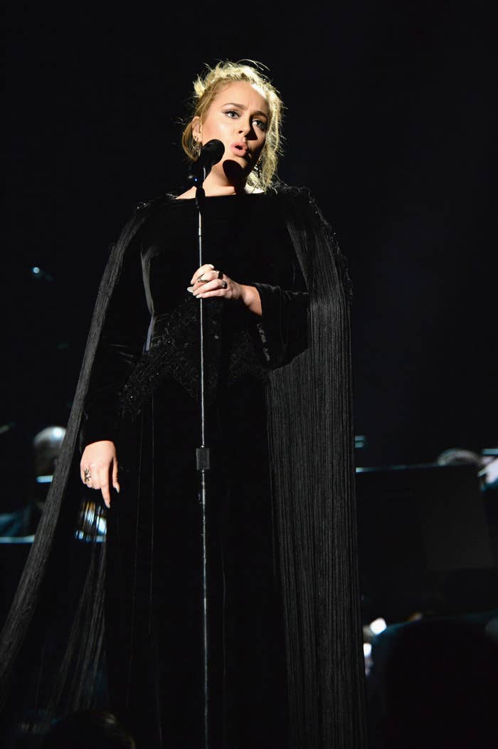 Adele performs on stage wearing a long, elegant black dress, holding a microphone