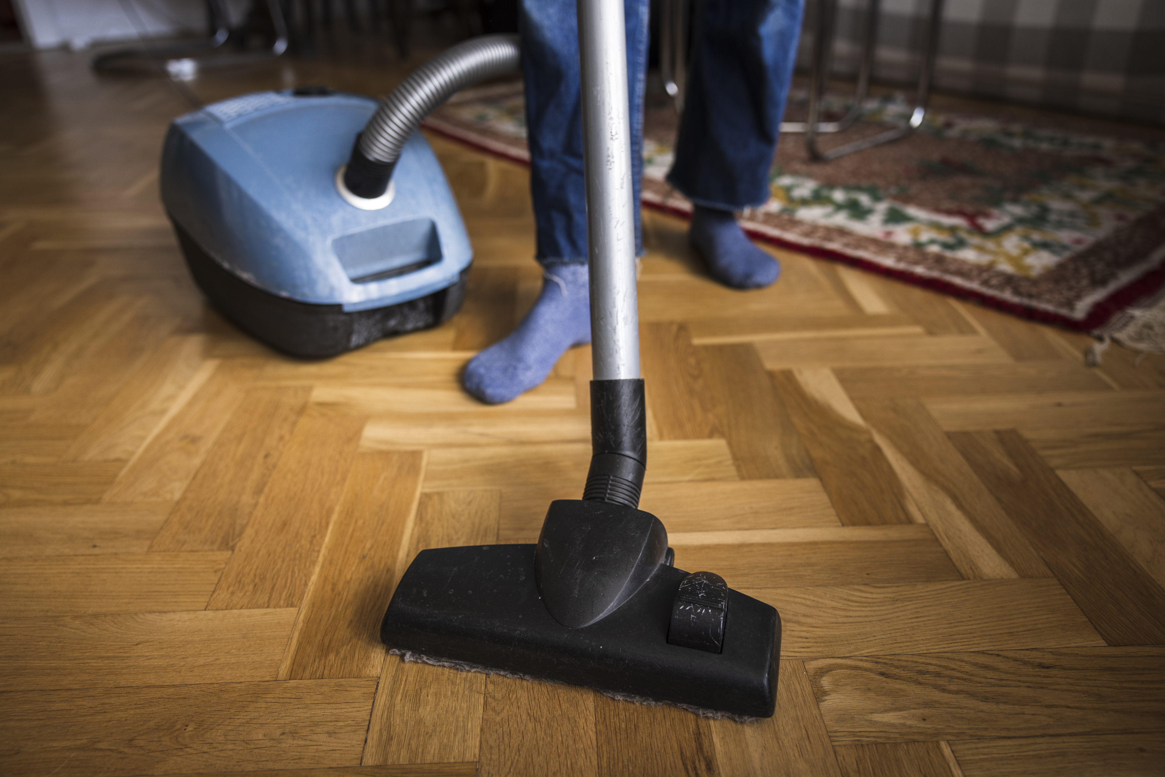 A person wearing blue socks vacuuming a wooden floor with a canister vacuum
