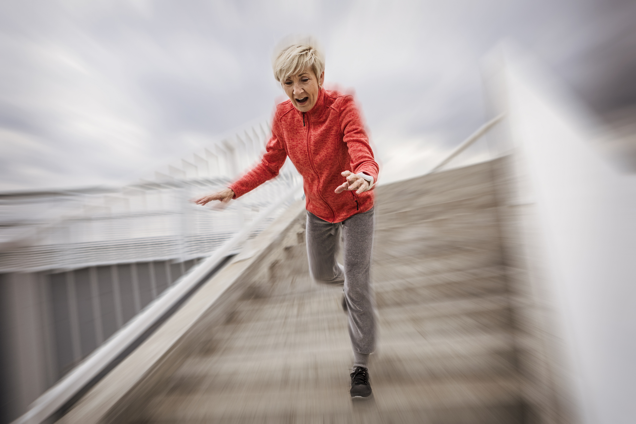 A person wearing a jacket, pants, and sneakers appears to be tripping while running down a set of stairs outside