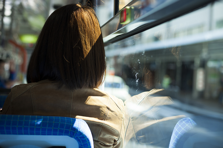 バスの中で窓の外を見つめる女性の後ろ姿。