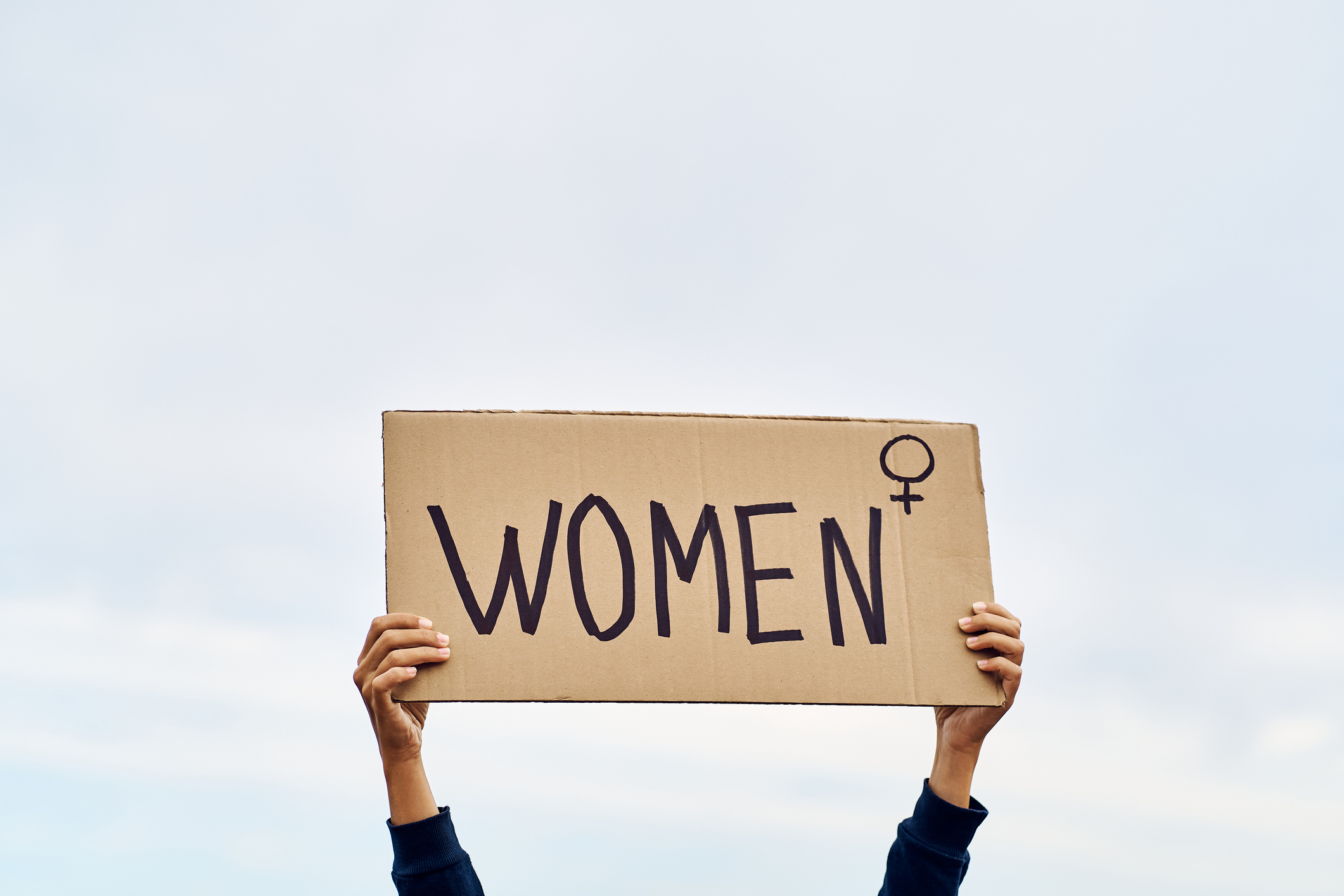 Two hands holding a cardboard sign that reads &quot;WOMEN&quot; with a female symbol next to it