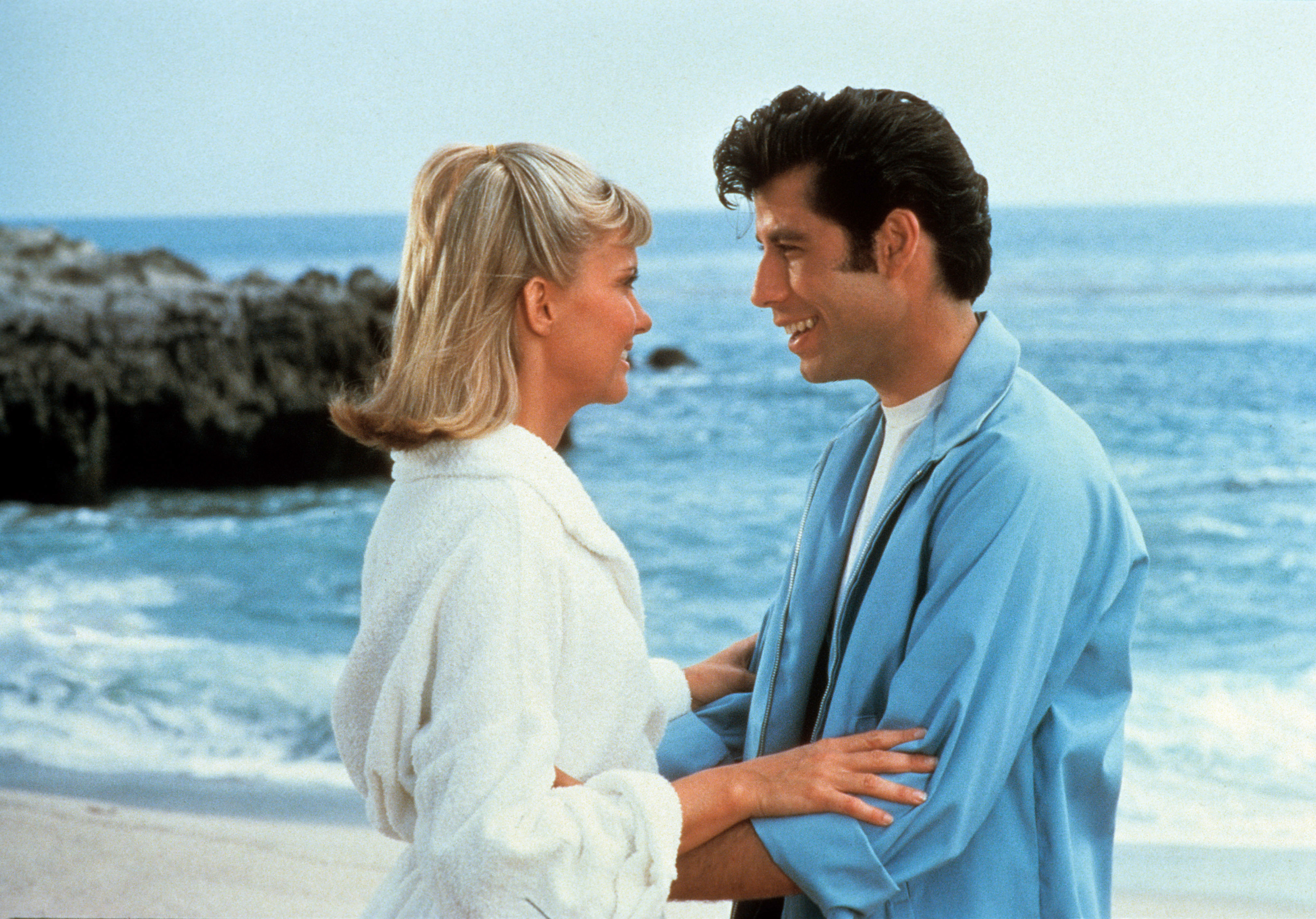 Olivia Newton-John and John Travolta embrace on a beach, smiling at each other, in a scene from the movie &quot;Grease.&quot;
