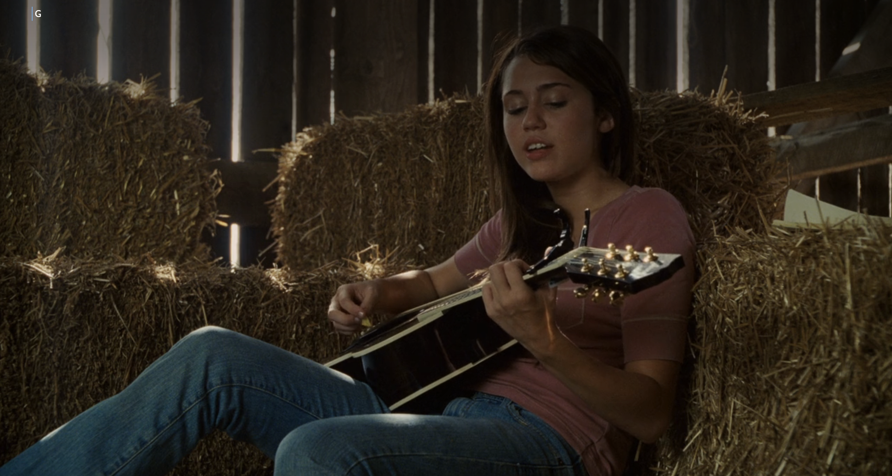 Miley Stewart (Miley Cyrus) plays the guitar while sitting on hay in a barn in a scene from &quot;Hannah Montana: The Movie.&quot;