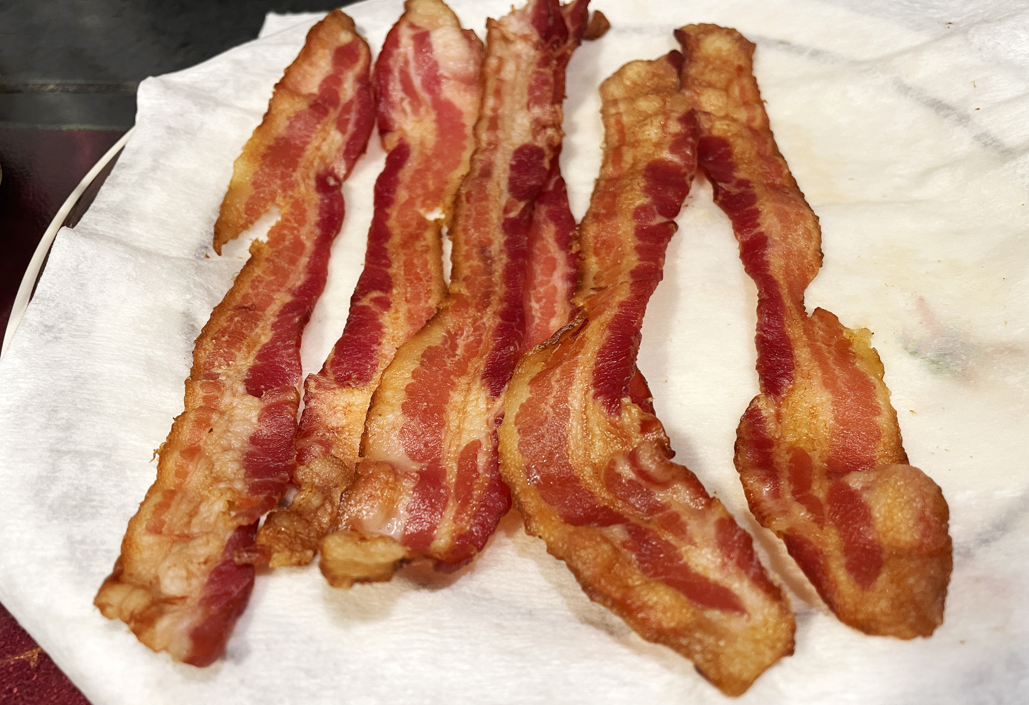 Several crispy, cooked bacon strips are laid out on a paper towel