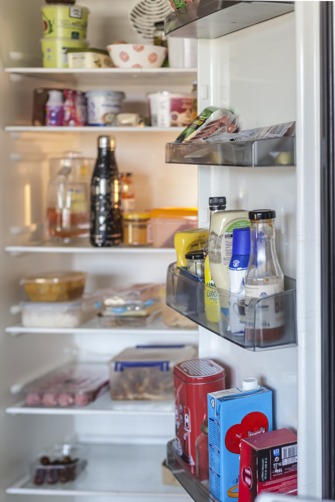 The image shows a neatly organized, open refrigerator filled with various foods, drinks, and condiments on the shelves and door compartments