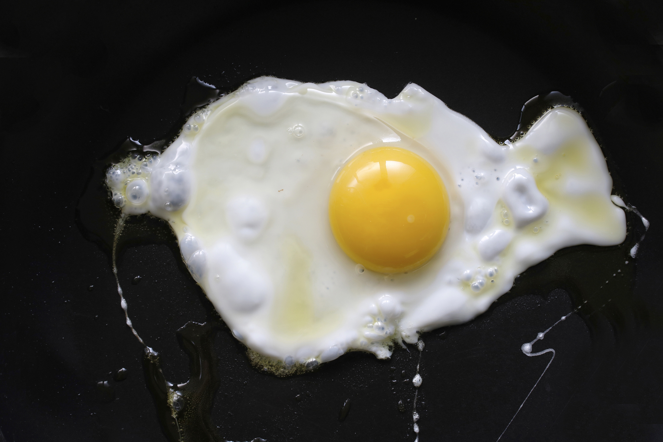 A close-up of a fried egg with a fully cooked white and a slightly runny yolk on a black surface