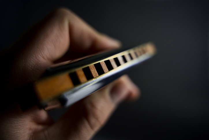 A close-up of a hand holding a harmonica with an emphasis on the instrument&#x27;s holes