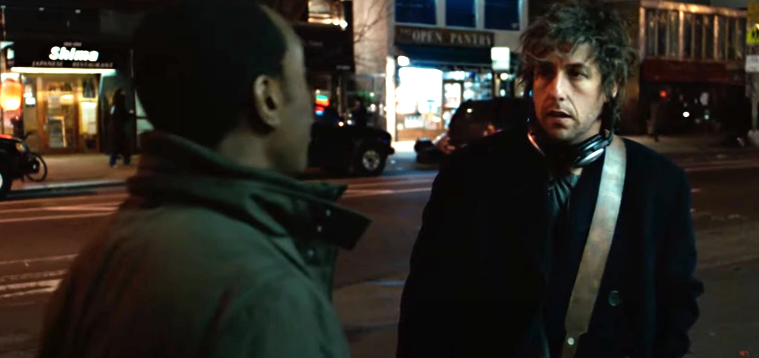 Don Cheadle and Adam Sandler in a scene, standing on a street at night, engaged in conversation